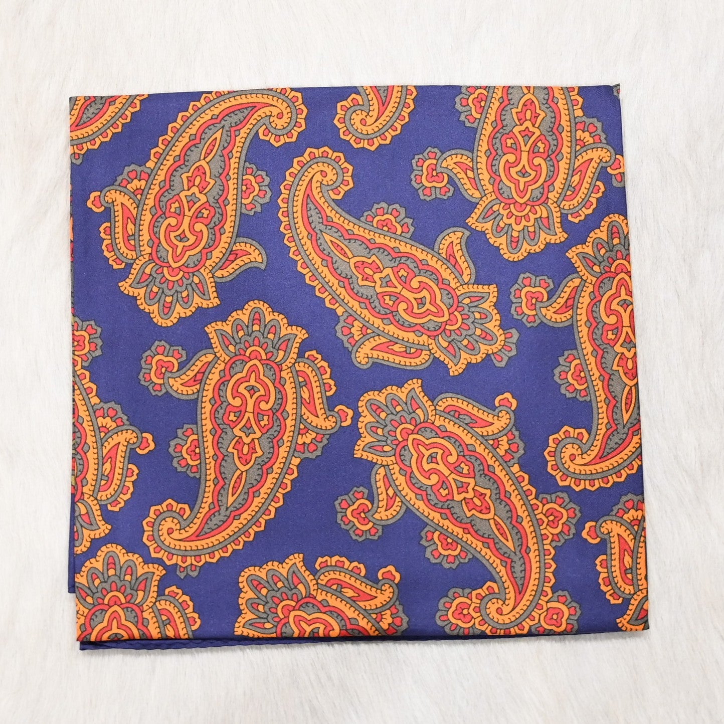 View of Schaefer paisley wild rag scarf in blue, orange and red with bold border and rolled edges