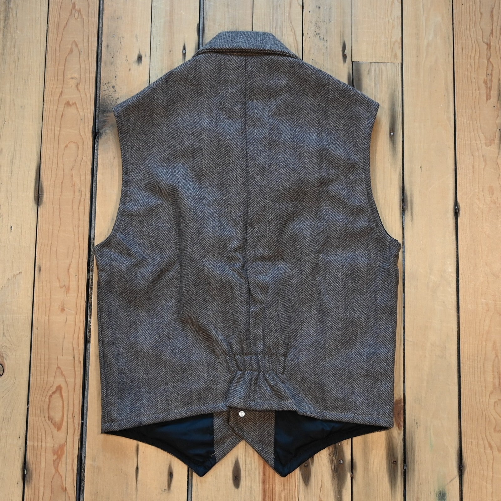 Taupe herringbone wool vest with lapel collar, running horse brass buttons, front and inside pockets, and hidden elastic back