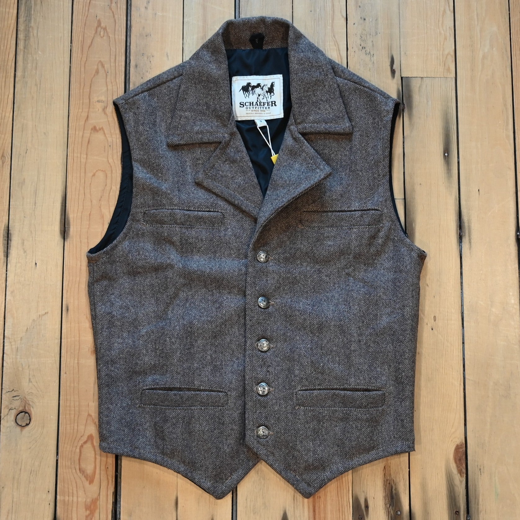 Taupe herringbone wool vest with lapel collar, running horse brass buttons, front and inside pockets, and hidden elastic back