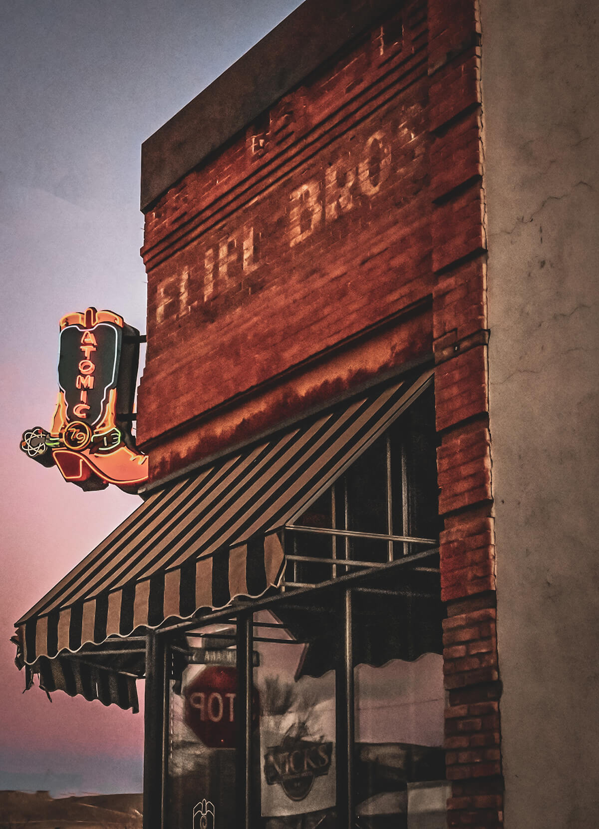 A photo of the neon cowboy boot sign for Atomic 79 on a brick building