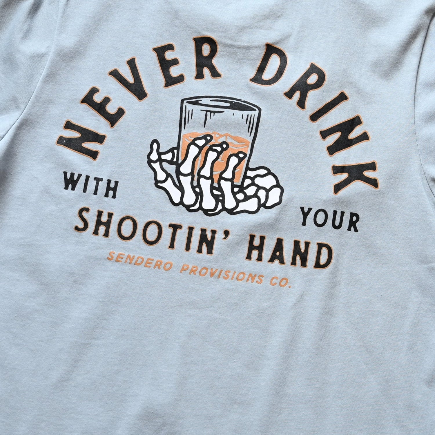 View of Sendero Big Sky Blue graphic tee with “Never drink with your shooting hand” print