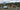 A photo of an old covered wagon next to a brown barn in a mountain valley