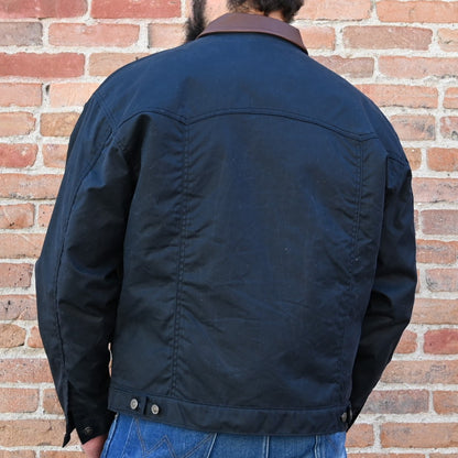 View of Schaefer black trucker jacket with leather collar, waxed canvas shell, and brass snaps