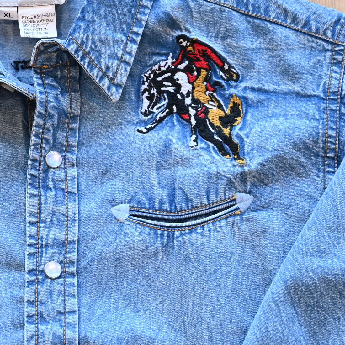 View of Rockmount kids denim shirt with bronc rider embroidery, piping, and snap western details
