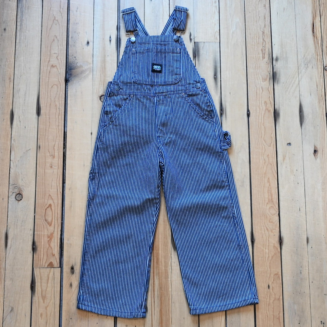 View of Front of kids KEY bib overall in blue denim and stripped.
