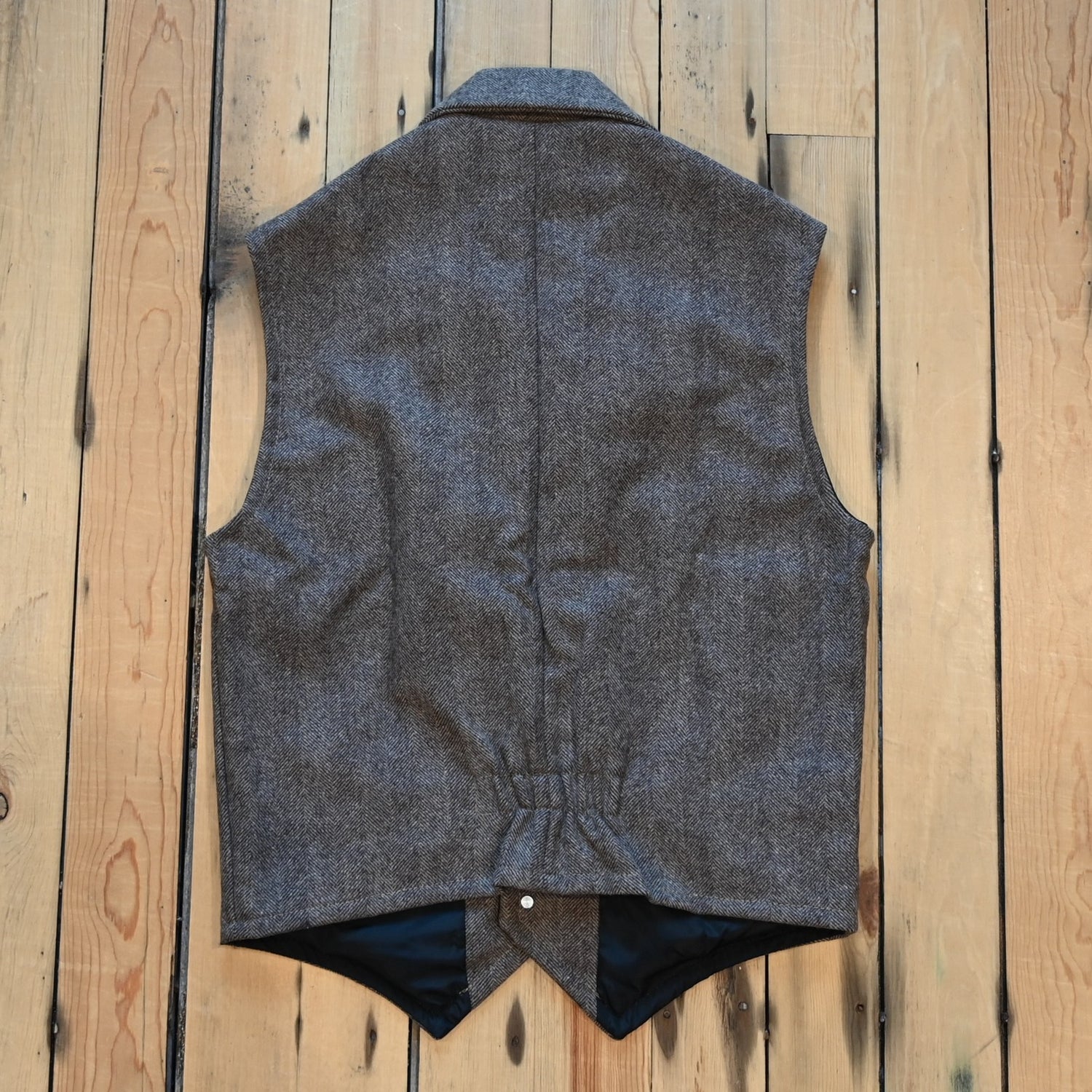 Taupe herringbone wool vest with lapel collar, running horse brass buttons, front and inside pockets, and hidden elastic back