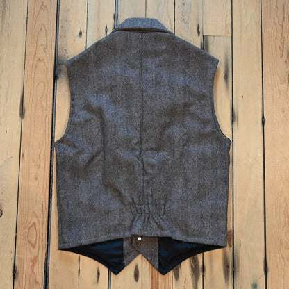 Taupe herringbone wool vest with lapel collar, running horse brass buttons, front and inside pockets, and hidden elastic back