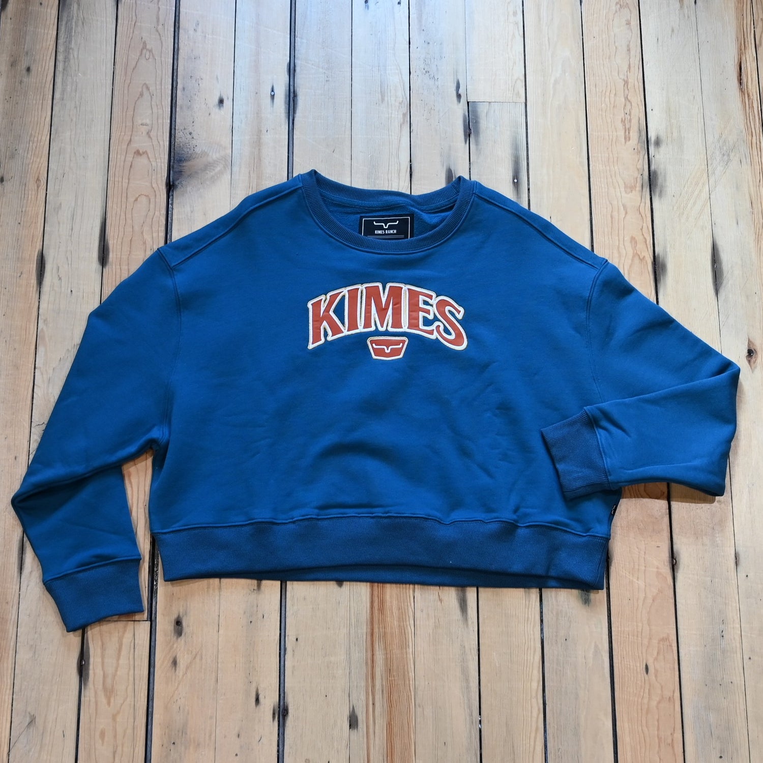 View of Kimes Ranch Ladies Colfax Crew Sweatshirt in Mid Blue, featuring an oversized fit, ribbed hem, and embroidered logo