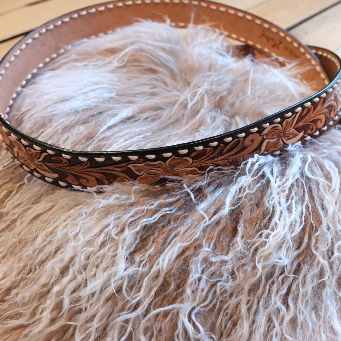 Close-up of floral tooled leather shoulder strap on a Morris Kaye fur handbag.