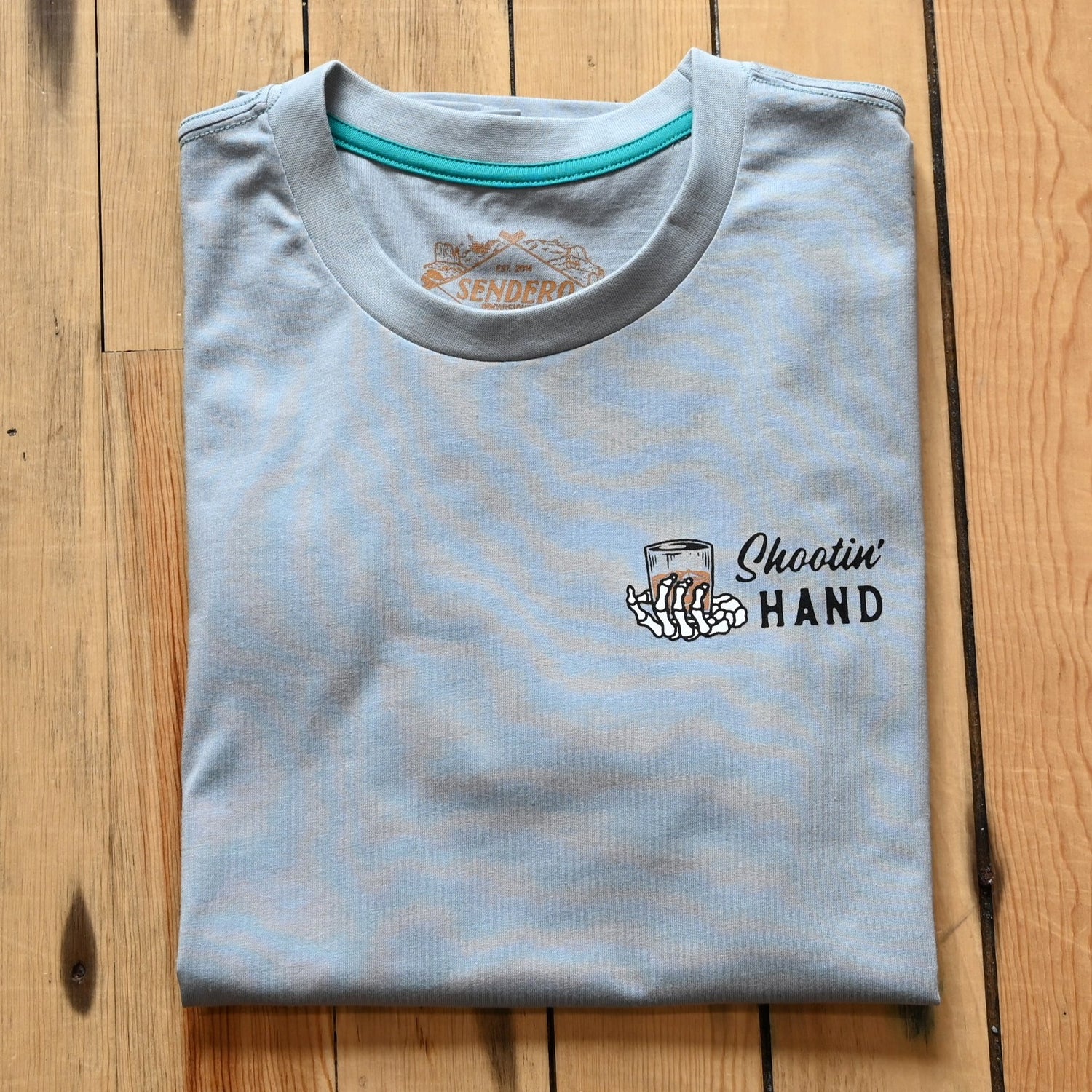 View of Sendero Big Sky Blue graphic tee with “Never drink with your shooting hand” print