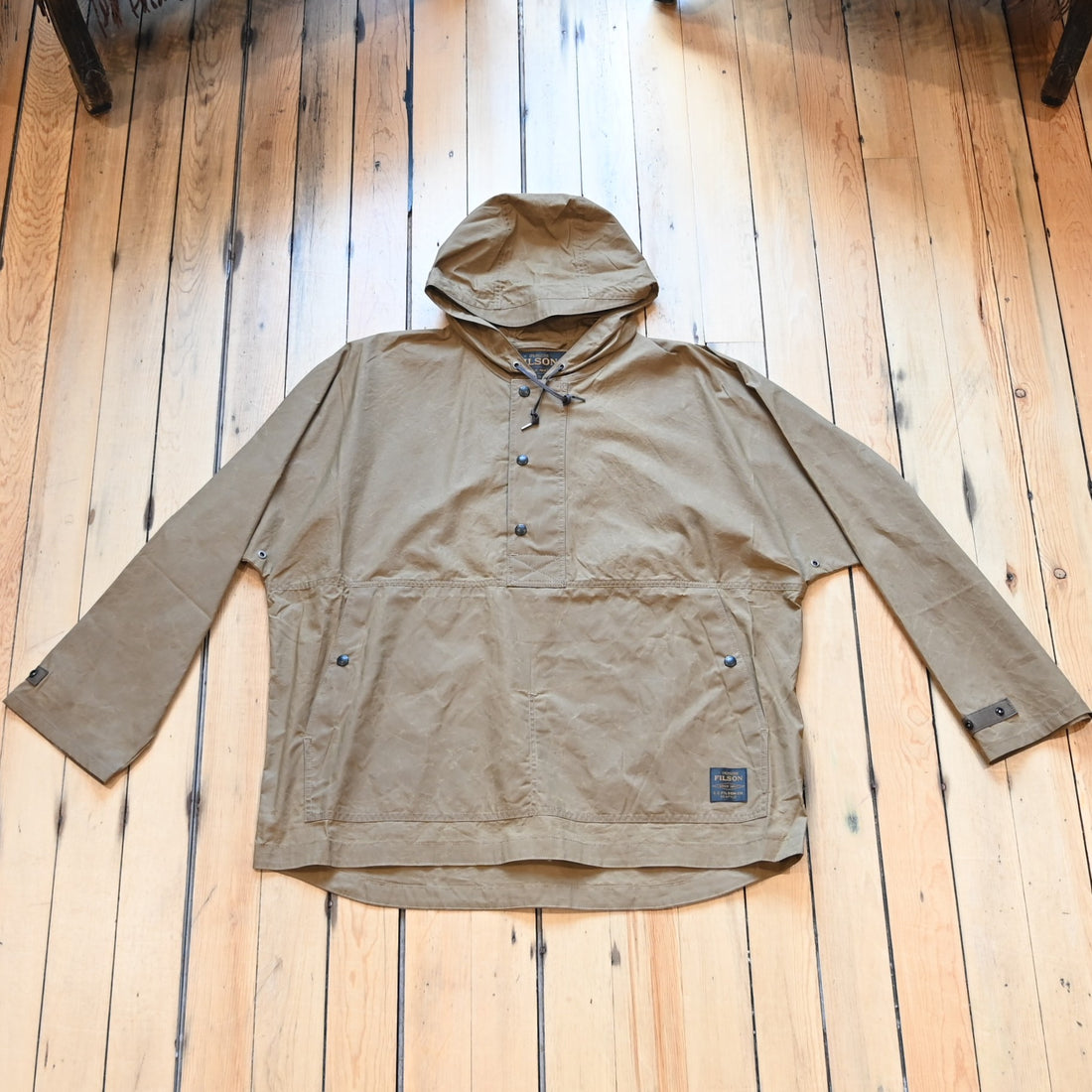 View of Filson Ranger Lightweight Anorak in Dark Beige, showcasing its waxed canvas fabric, adjustable hood, and snap-secure storm flap