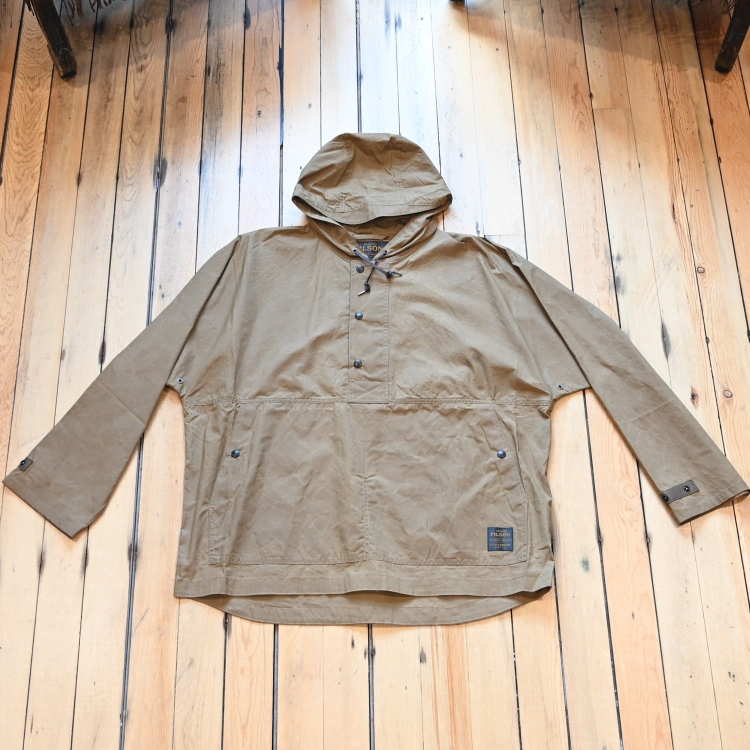 View of Filson Ranger Lightweight Anorak in Dark Beige, showcasing its waxed canvas fabric, adjustable hood, and snap-secure storm flap
