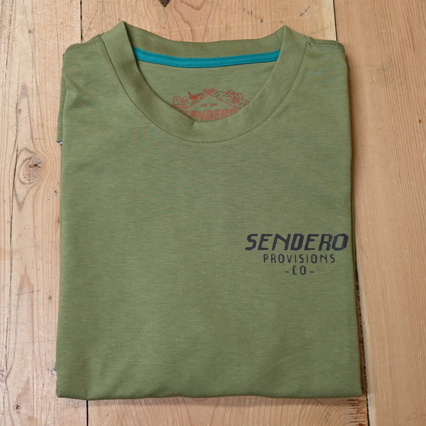 View of Sendero sage green Triceratops T-Shirt with cowboy roping a dinosaur graphic