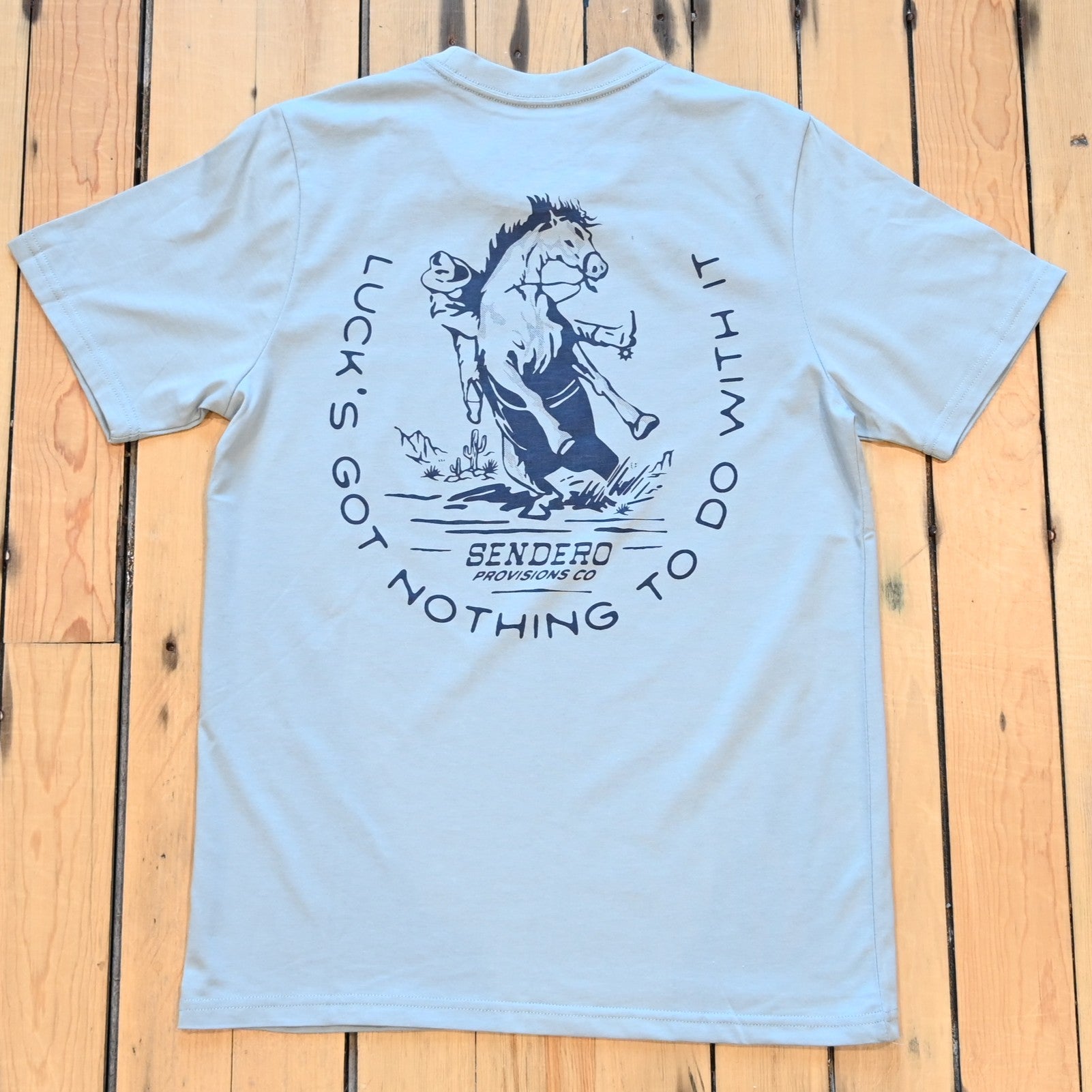 Big Sky Blue No Luck T-Shirt by Sendero with bucking horse graphic and “Luck’s Got Nothin’ to Do With It” text