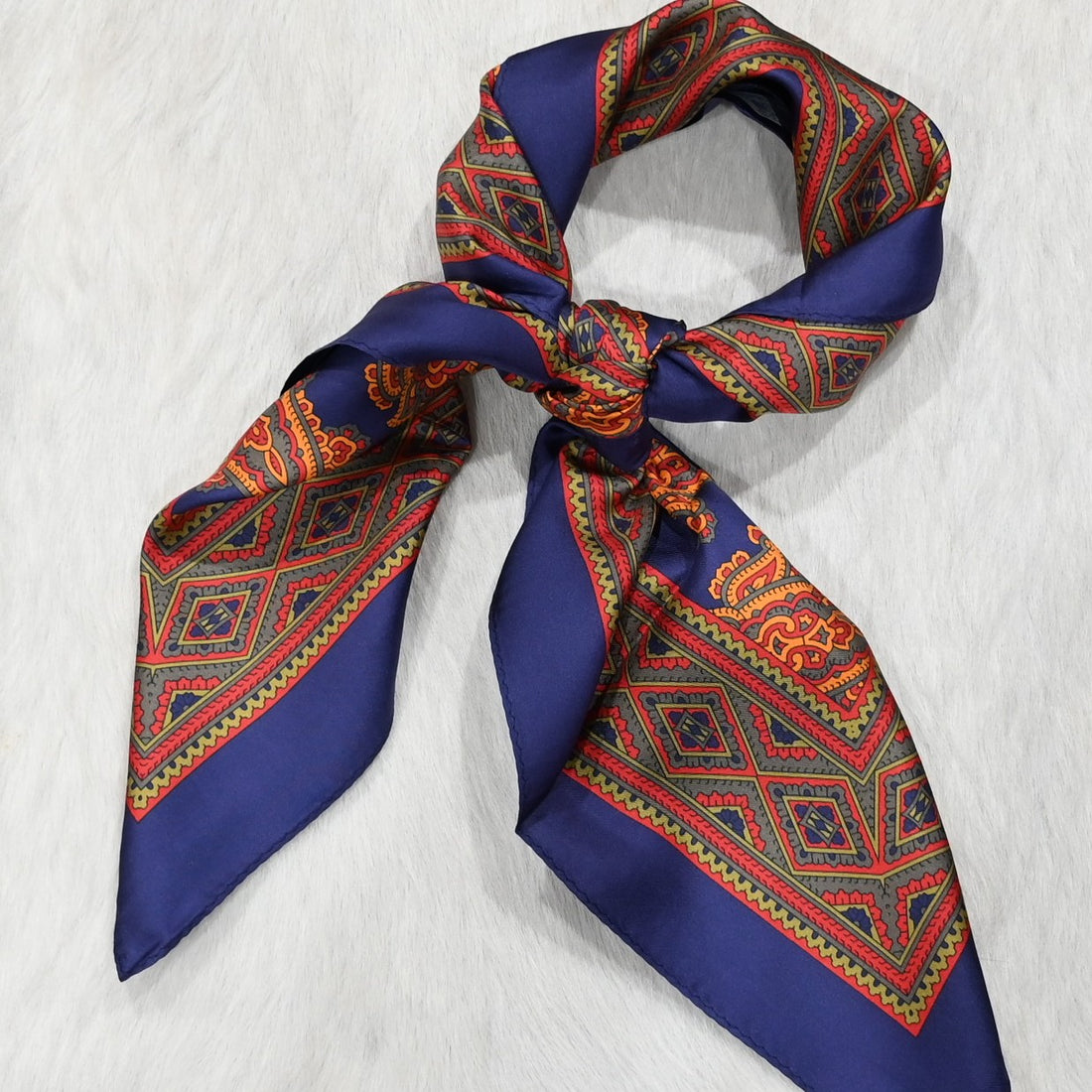 View of Schaefer paisley wild rag scarf in blue, orange and red with bold border and rolled edges