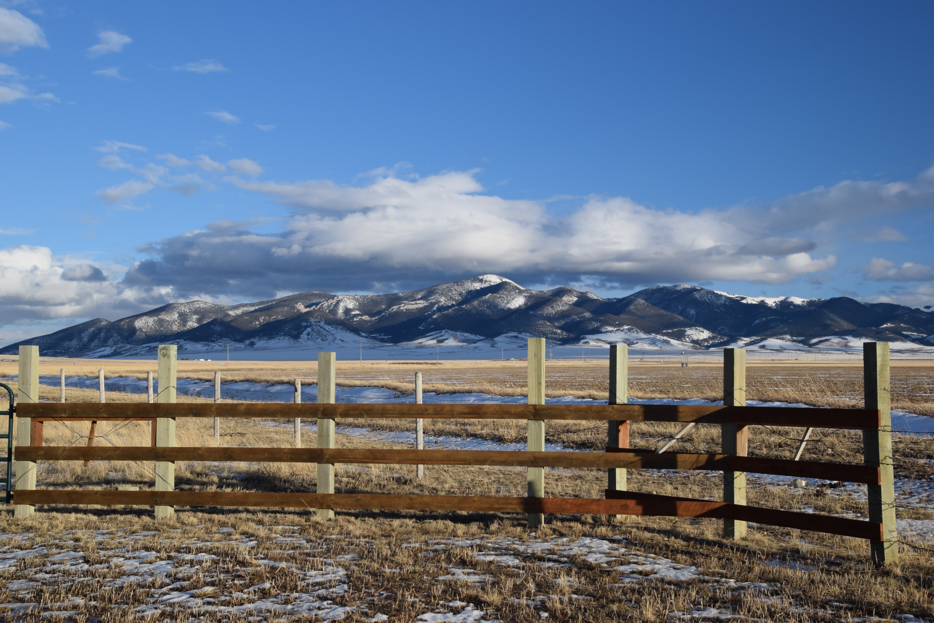 A photo of a rustic fence overlooking a snowy field and dramatic mountain range