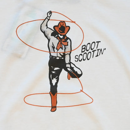 Ladies vintage white Boot Scootin’ boxy tee by Sendero with cowgirl roping graphic and cropped fit