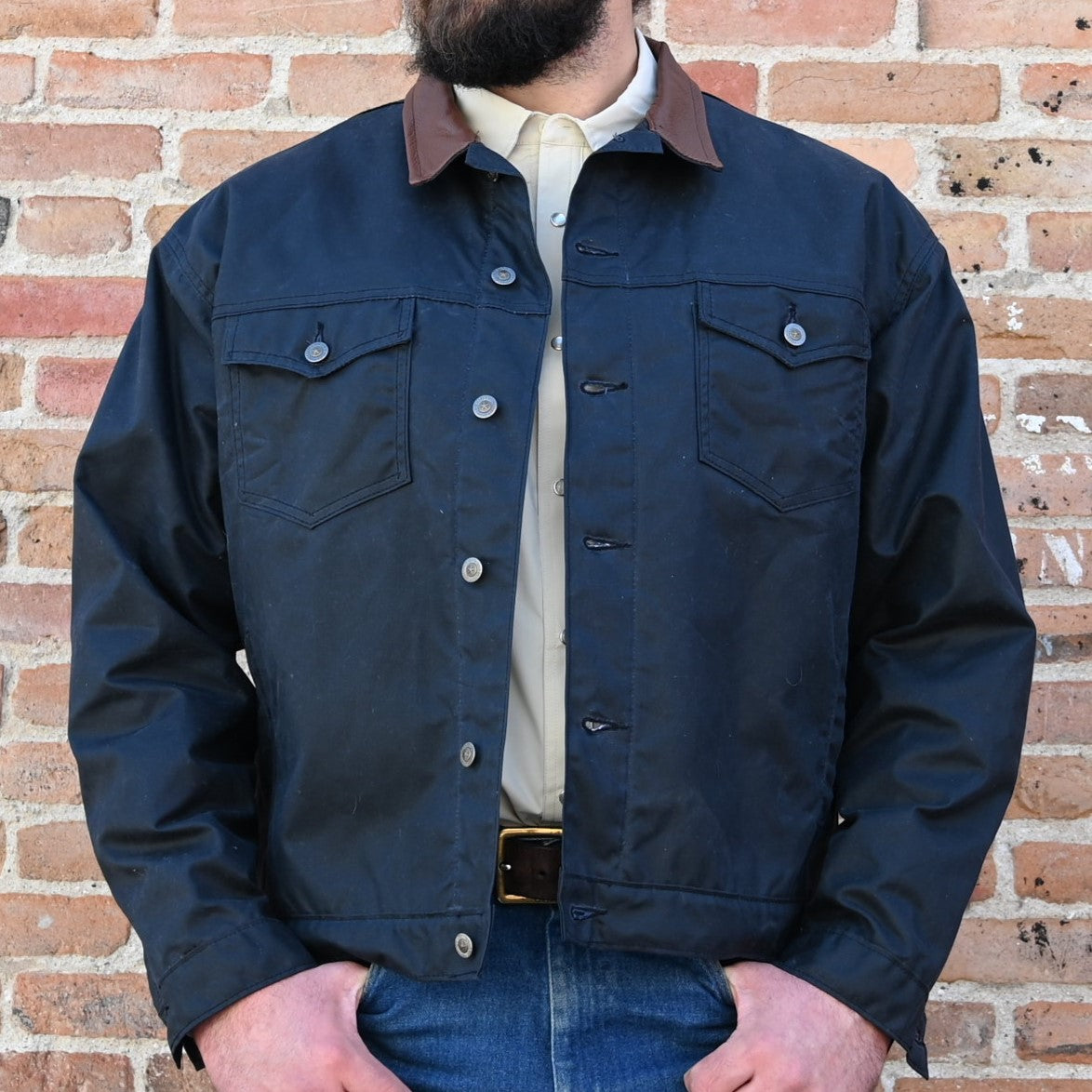 View of Schaefer black trucker jacket with leather collar, waxed canvas shell, and brass snaps