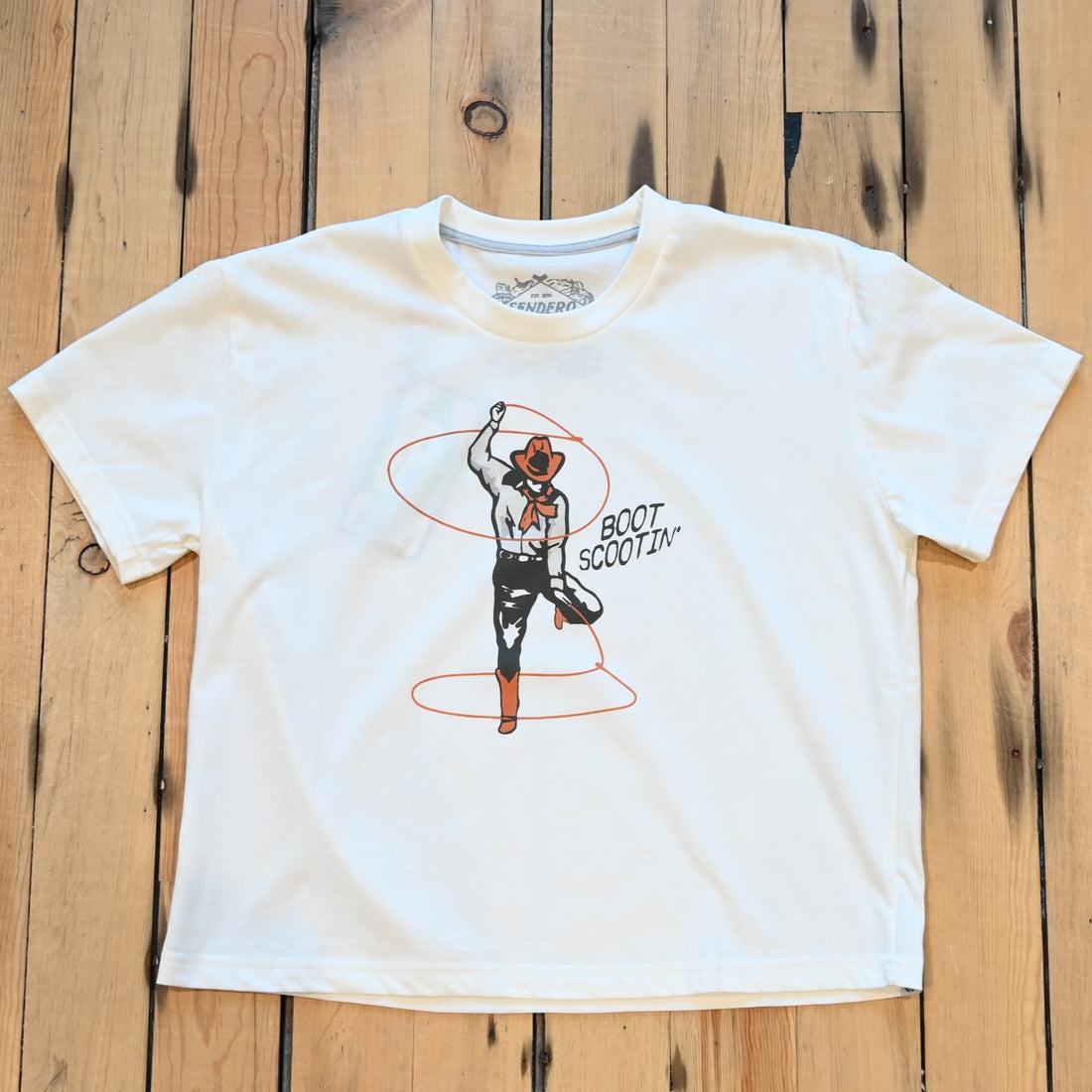 Ladies vintage white Boot Scootin’ boxy tee by Sendero with cowgirl roping graphic and cropped fit