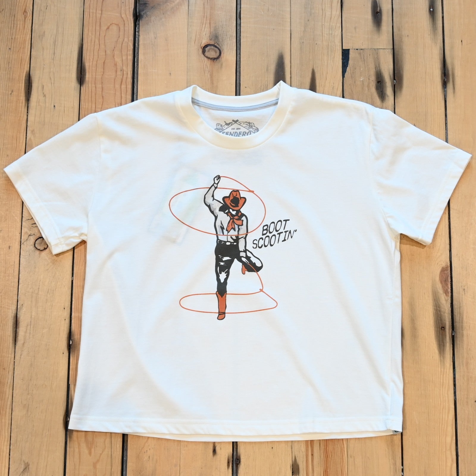 Ladies vintage white Boot Scootin’ boxy tee by Sendero with cowgirl roping graphic and cropped fit
